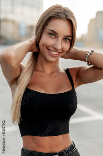 Fototapeta Naklejka Na Ścianę i Meble -  Happy young woman with pretty smile in black t-shirt for design mockup with jewelry bracelet on hand walks on the street