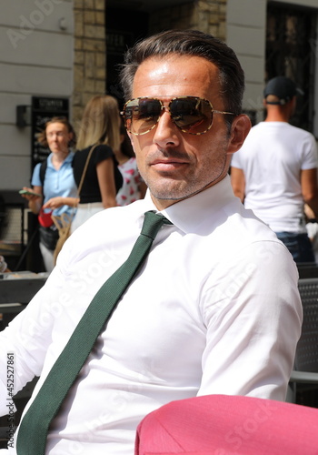 Bardzo przystojny, elegancki mężczyzna w białej koszuli i zielonym krawacie i okularach przeciwsłonecznych.