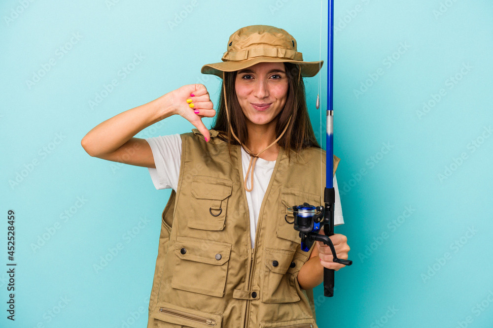 Young caucasian fisherwoman isolated on blue background showing a dislike gesture, thumbs down. Disagreement concept. Young caucasian fisherwoman isolated on blue background showing a dislike gesture, thumbs down. Disagreement concept.