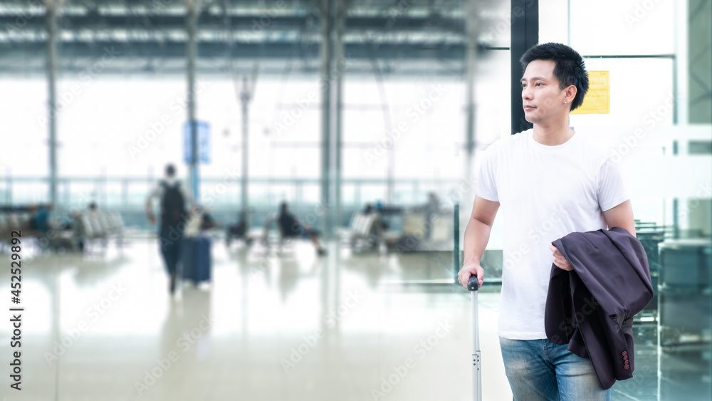 Young Asian traveling backpacker, Travel concept, man smiling happy near window at the airport and watching plane before departure. He is standing and carrying luggage.