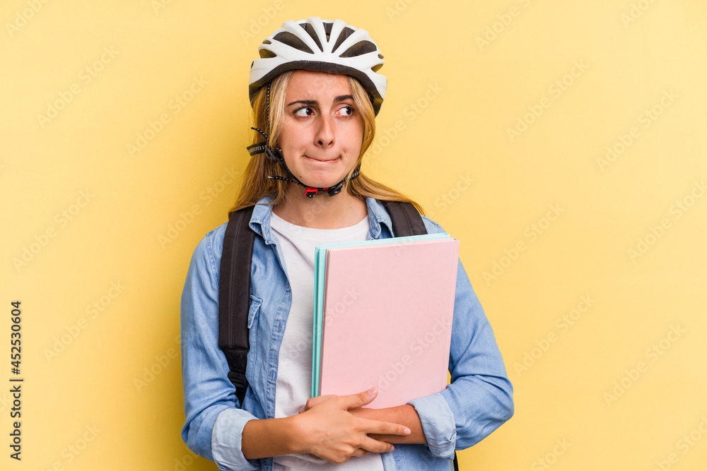 Young caucasian student woman wearing a bike helmet isolated on yellow background confused, feels doubtful and unsure. Young caucasian student woman wearing a bike helmet isolated on yellow background confused, feels doubtful and unsure.