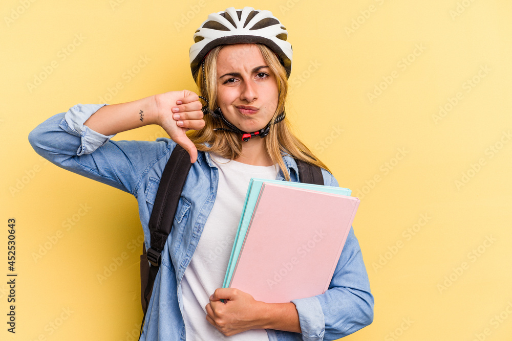 Young caucasian student woman wearing a bike helmet isolated on yellow background showing a dislike gesture, thumbs down. Disagreement concept. Young caucasian student woman wearing a bike helmet isolated on yellow background showing a dislike gesture, thumbs down. Disagreement concept.