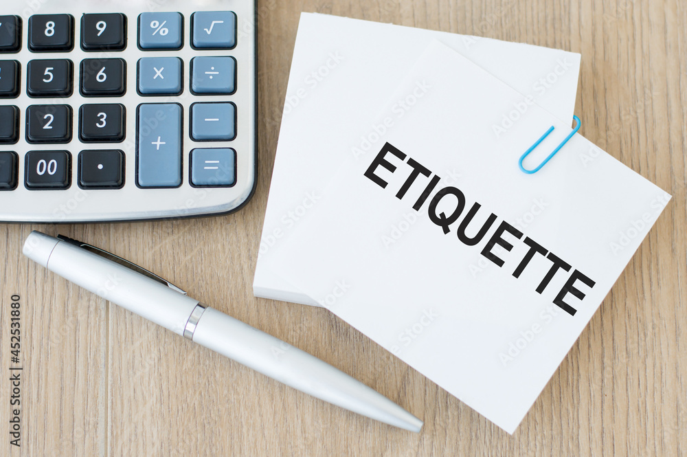 a business card with the inscription ETIQUETTE, next to a silver pen and a calculator on a wooden table. A business concept. a business card with the inscription ETIQUETTE, next to a silver pen and a calculator on a wooden table. A business concept.