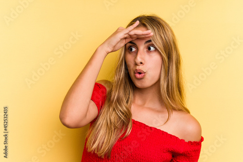 Young caucasian blonde woman isolated on yellow background looking far away keeping hand on forehead.