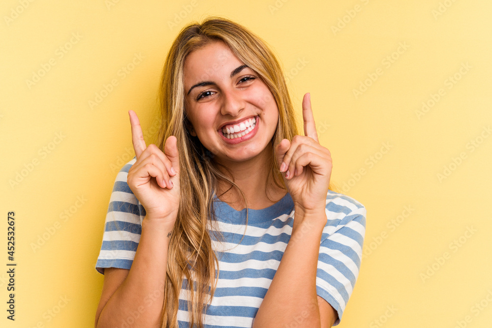 Young caucasian blonde woman isolated on yellow background pointing to different copy spaces, choosing one of them, showing with finger. Young caucasian blonde woman isolated on yellow background pointing to different copy spaces, choosing one of them, showing with finger.