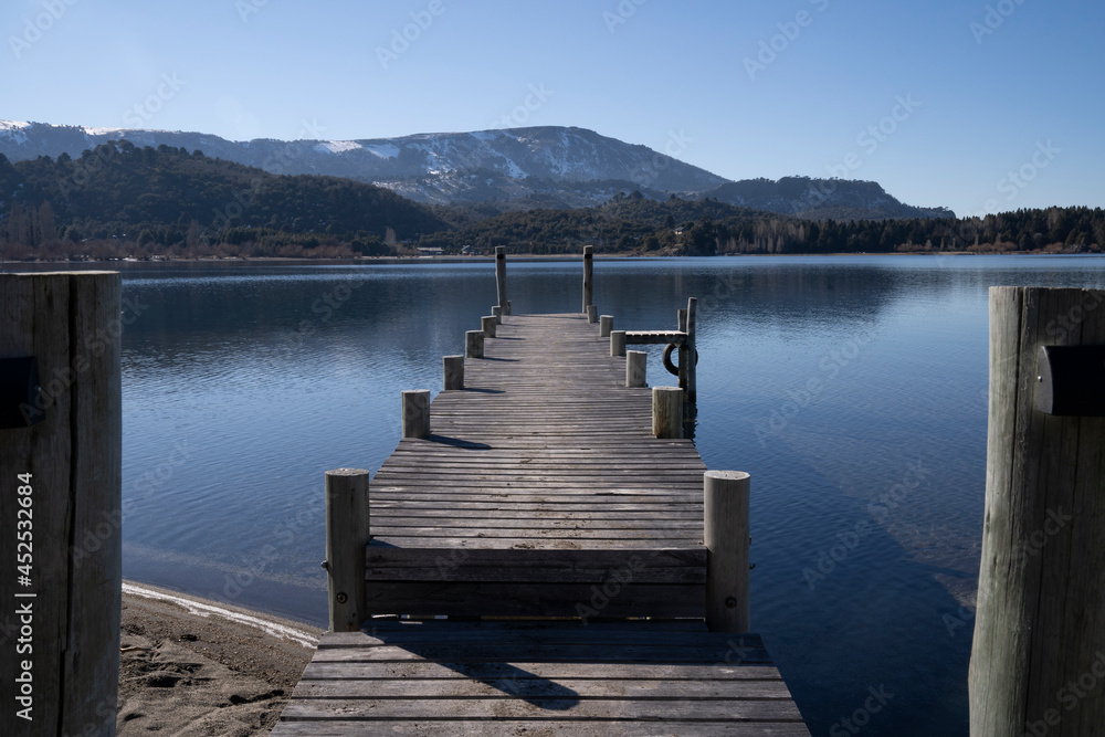The wooden docks in the placid lake. View of the blue sky, forest and mountains reflection in the water.
