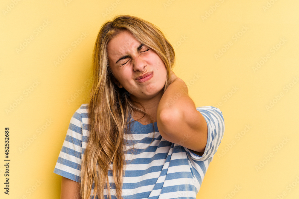 Young caucasian blonde woman isolated on yellow background having a neck pain due to stress, massaging and touching it with hand. Young caucasian blonde woman isolated on yellow background having a neck pain due to stress, massaging and touching it with hand.