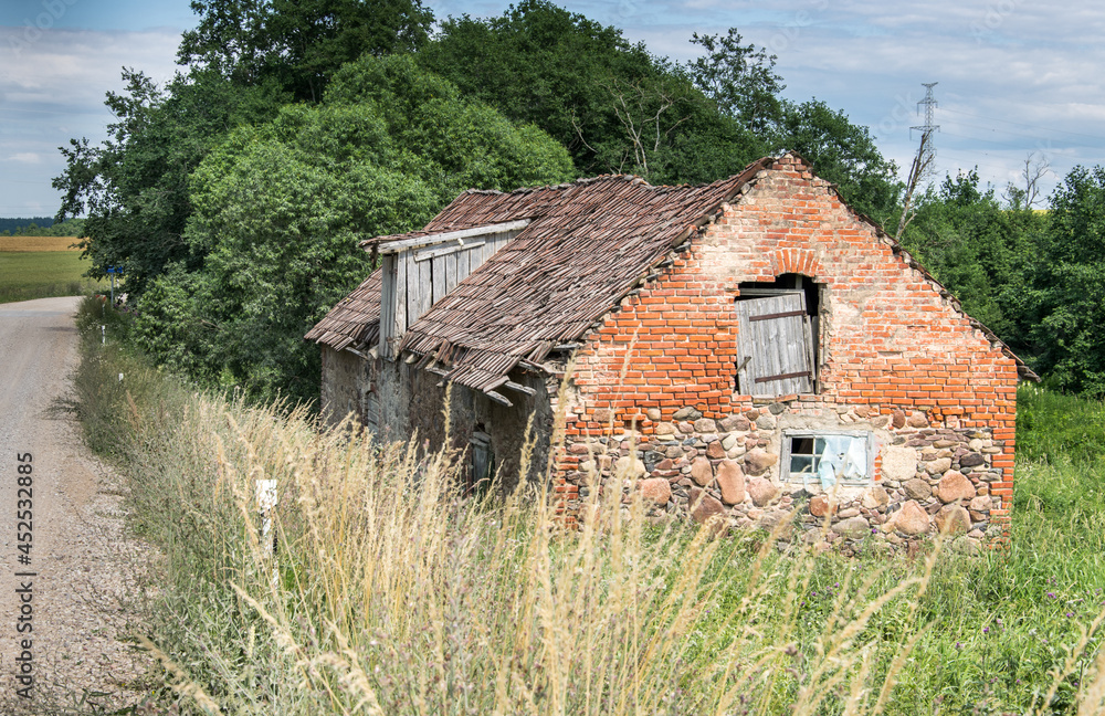 Fototapeta premium Old crumbling barn with a stone and red brick tiled roof in Latvia.