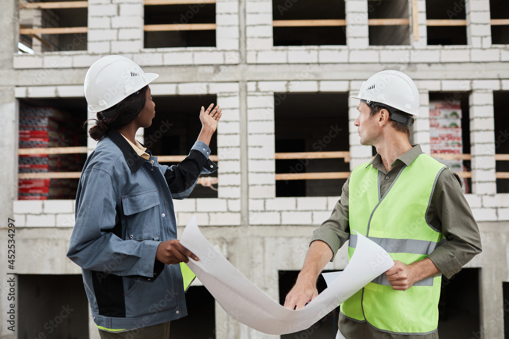 Side view portrait of two engineeers wearing hardhats at construction site Side view portrait of two engineeers wearing hardhats at construction site