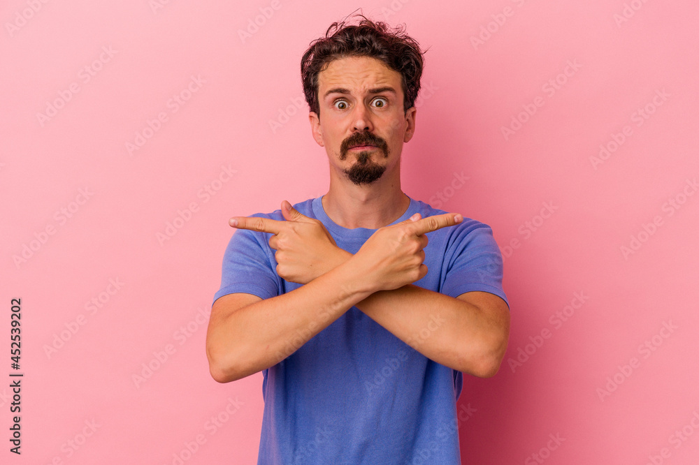 Young caucasian man isolated on pink background points sideways, is trying to choose between two options. Young caucasian man isolated on pink background points sideways, is trying to choose between two options.