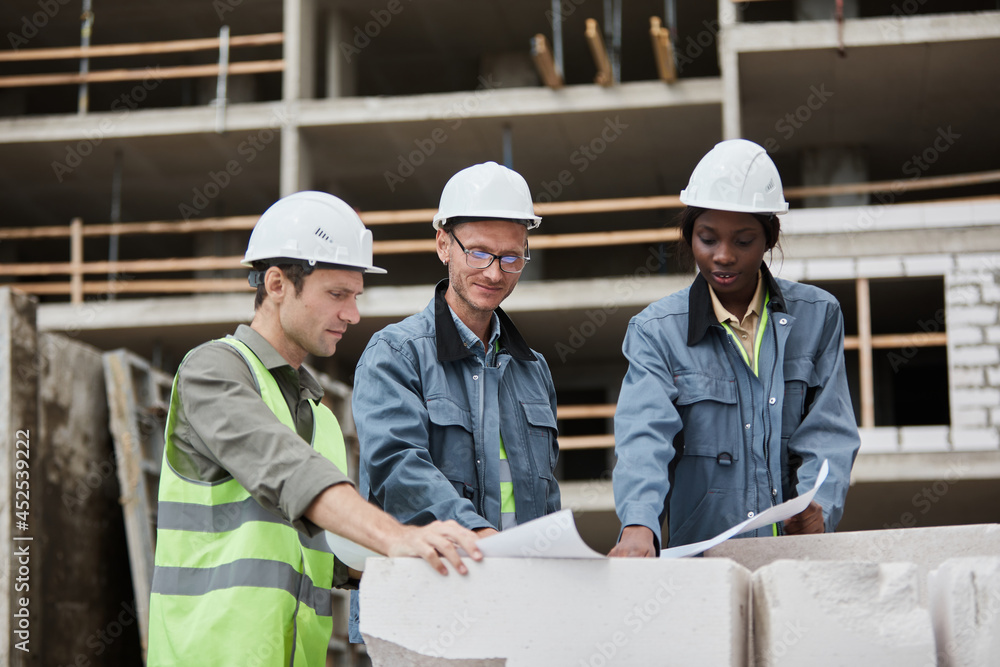 Waist up portrait of workers discussing floor plans at construction site, copy space Waist up portrait of workers discussing floor plans at construction site, copy space