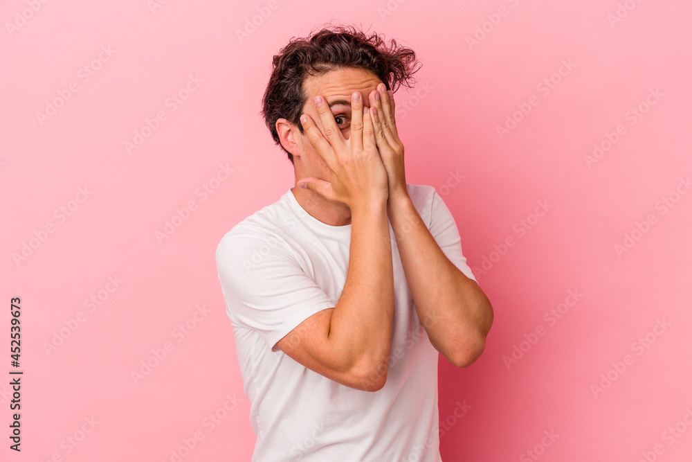 Young caucasian man isolated on pink background blink through fingers frightened and nervous. Young caucasian man isolated on pink background blink through fingers frightened and nervous.