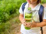 Thirsty boy holds in hands reusable green bottle with pure water. Summer outdoor recreation. Healthy lifestyle.