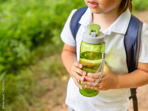 Thirsty boy holds in hands reusable green bottle with pure water. Summer outdoor recreation. Healthy lifestyle.