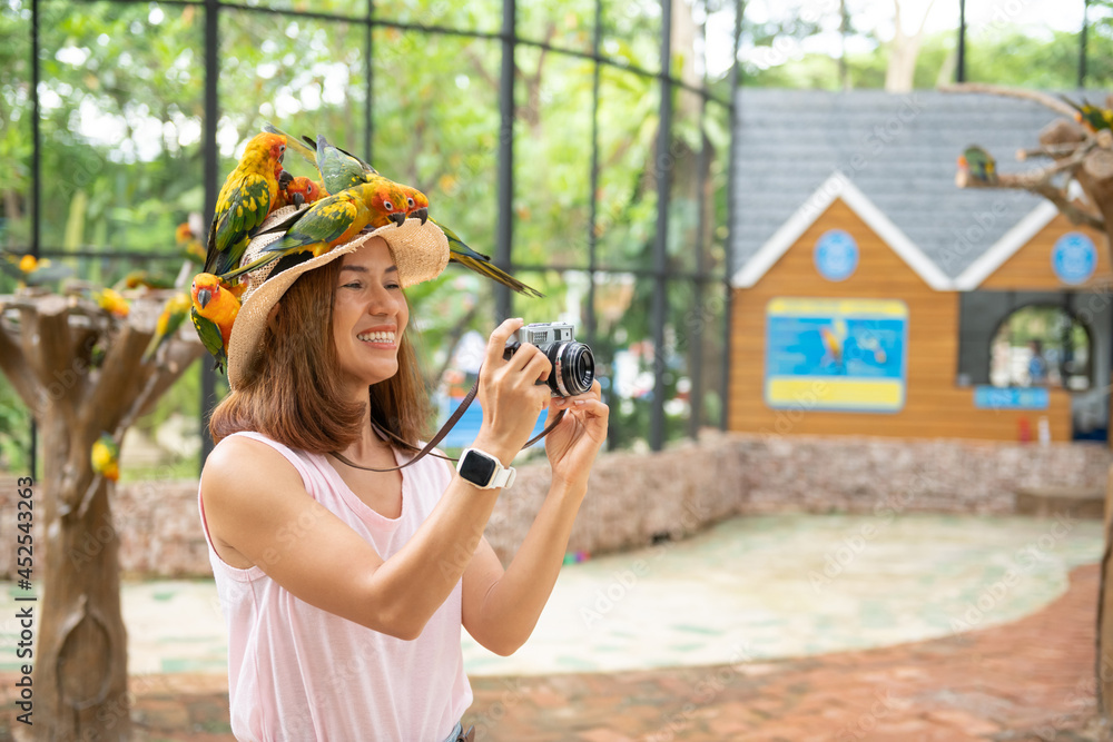 Asian beautiful woman enjoying with love bird on hand and body, in cage background, Environment human and nature concept, Smiling woman playing with her bird pet, Sun Conure parrot bird group.
