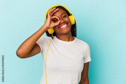Wallpaper Mural Young African American woman listening to music isolated on blue background  excited keeping ok gesture on eye. Torontodigital.ca