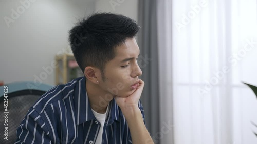 close up asian male freelancer is propping his head and murmuring to himself while looking into the space considering word choice in the living room at home.