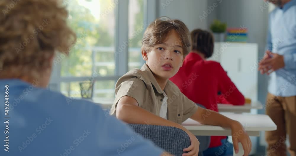 Back view of schoolboy sitting at desk on exam and turn around talking to classmate Back view of schoolboy sitting at desk on exam and turn around talking to classmate