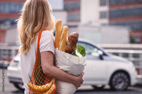 Woman with groceries walks to her car in a supermarket parking lot. Customer with reusable bags honor a sustainable lifestyle with zero waste and plastic free shopping photo