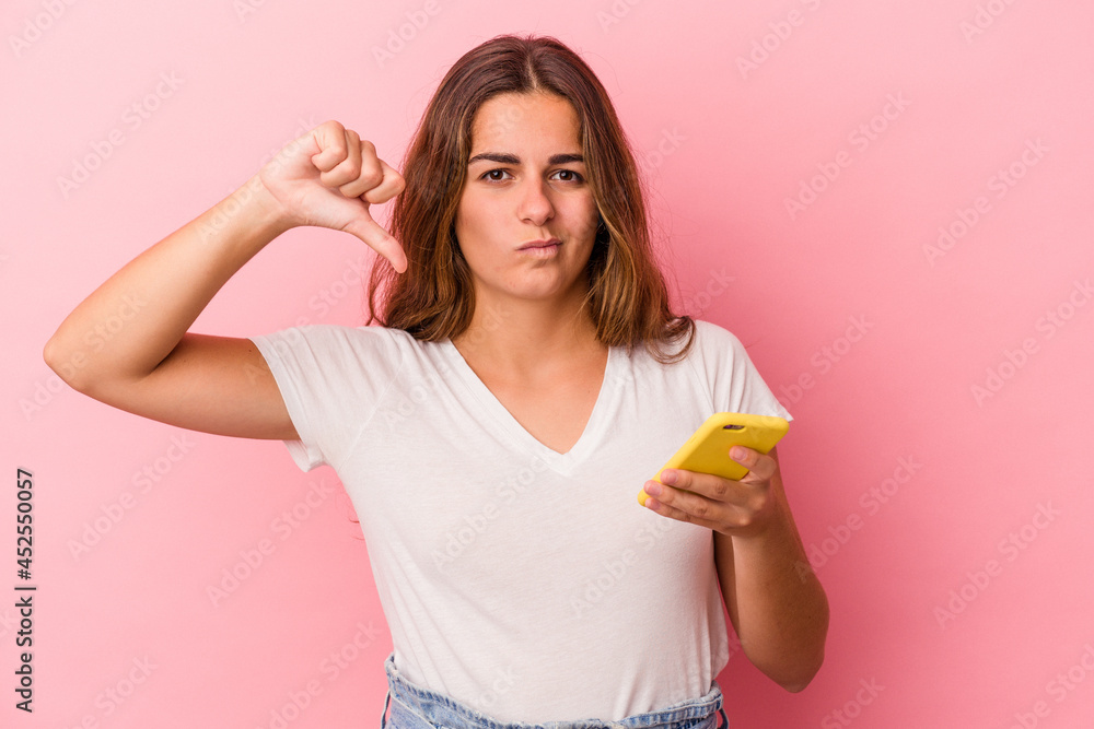 Young caucasian woman using mobile phone isolated on pink background  showing a dislike gesture, thumbs down. Disagreement concept.