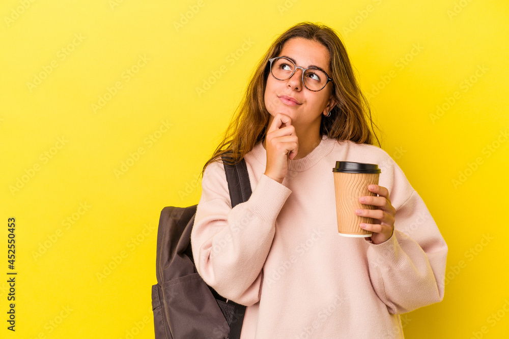 Young caucasian student woman holding coffee isolated on yellow background looking sideways with doubtful and skeptical expression. Young caucasian student woman holding coffee isolated on yellow background looking sideways with doubtful and skeptical expression.