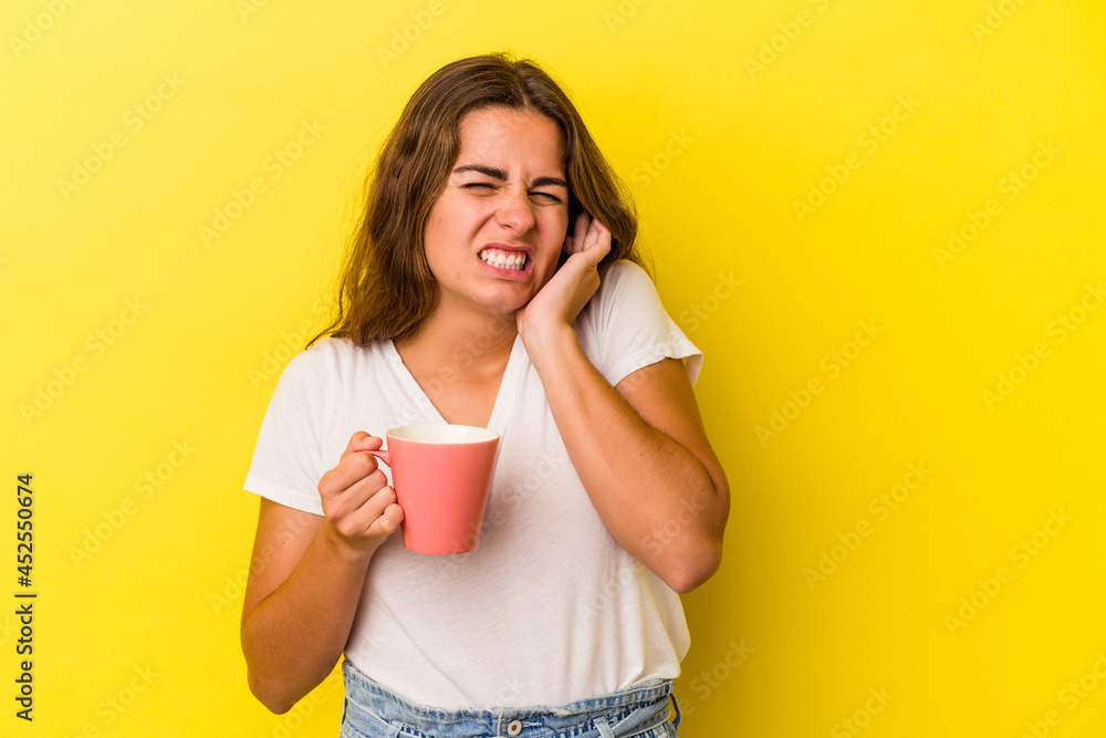 Young caucasian woman holding a mug isolated on yellow background covering ears with hands. Young caucasian woman holding a mug isolated on yellow background covering ears with hands.