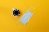 top view of cup of coffee and medical face mask on yellow isolated background