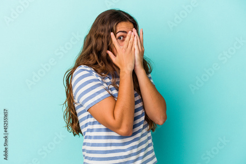 Young caucasian woman isolated on blue background  blink through fingers frightened and nervous. © Asier
