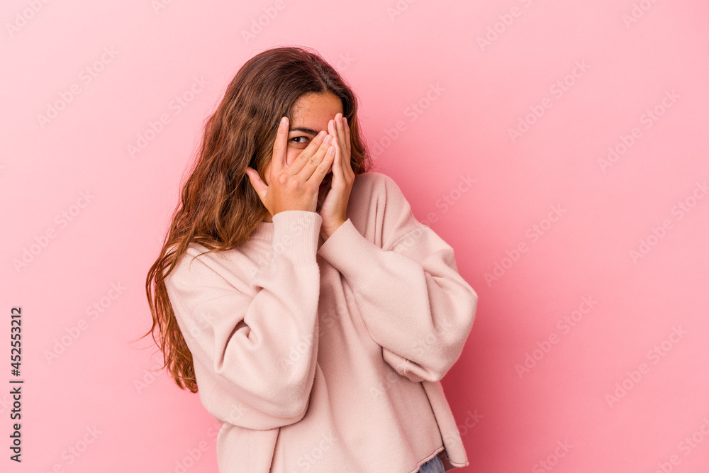 Young caucasian woman isolated on pink background blink at the camera through fingers, embarrassed covering face. Young caucasian woman isolated on pink background blink at the camera through fingers, embarrassed covering face.
