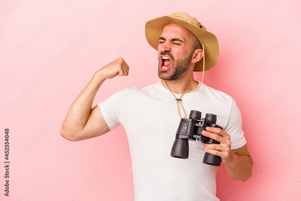 Young caucasian bald man holding binoculars isolated on pink background raising fist after a victory, winner concept. Young caucasian bald man holding binoculars isolated on pink background raising fist after a victory, winner concept.