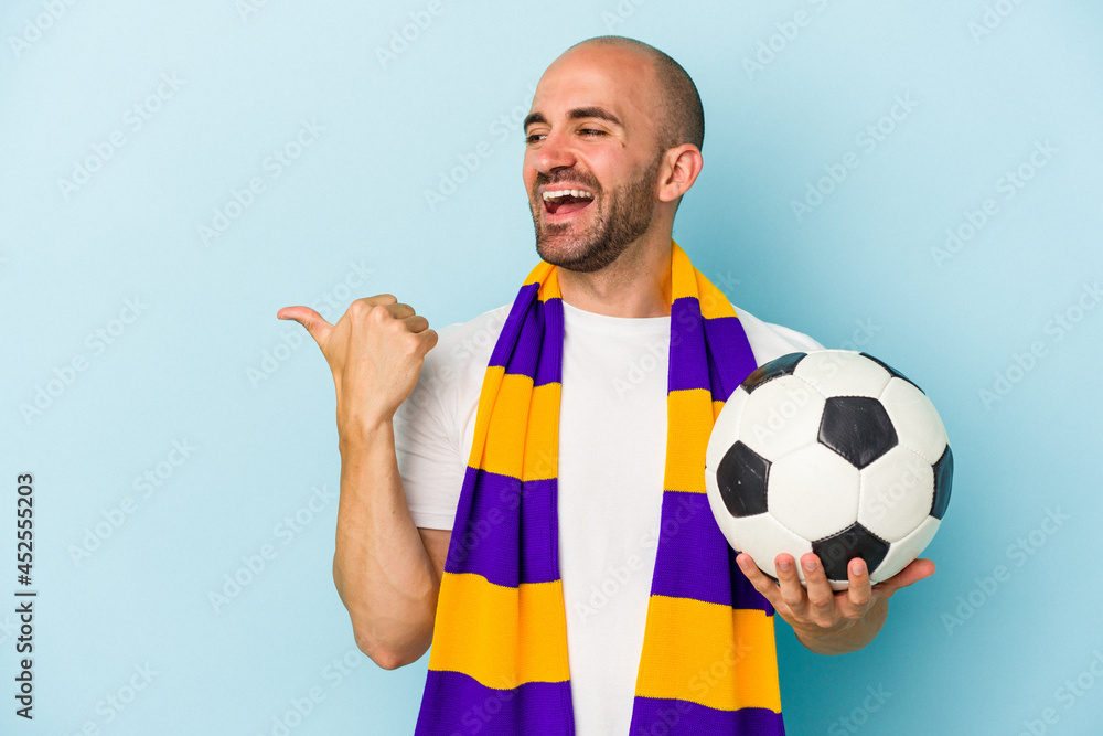 Young sport bald man wearing a scarf isolated on blue background  points with thumb finger away, laughing and carefree.