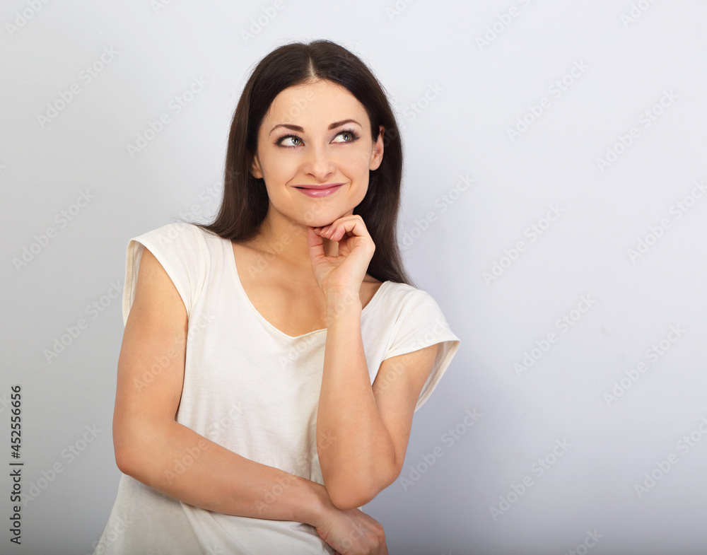 Beautiful young casual cute smiling woman on blue background looking up and thinking. Closeup portrait Beautiful young casual cute smiling woman on blue background looking up and thinking. Closeup portrait