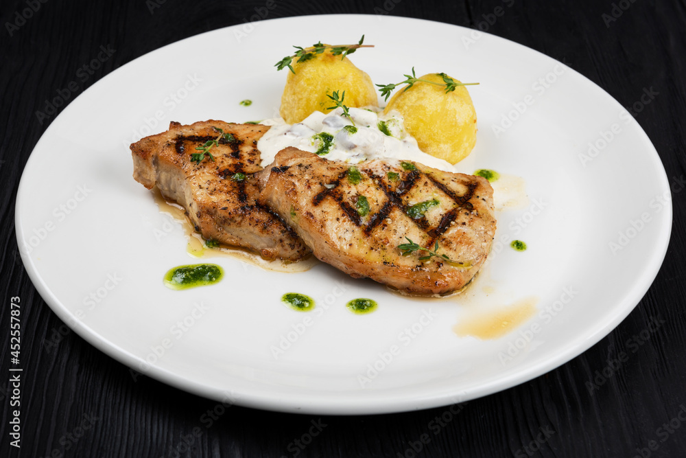 Grilled pork meat with mushroom sauce and potato on white plate on wooden black background Grilled pork meat with mushroom sauce and potato on white plate on wooden black background
