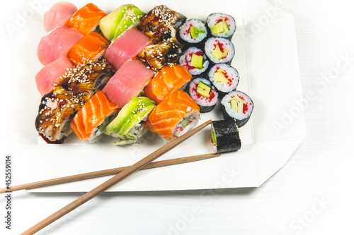 Man takes Tasty Colorful assorted Set of different type Sushi with chopsticks. Dinner in Japanese style. Healthy food. Filadelfia and Maki sushi rolls with Avocado, Tuna, Salmon, fish and Prawns.