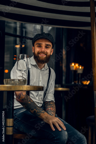 Young bearded man in a cafe on the street with a glass of wine. Romantic guy in a white shirt cap and suspenders in the city. Peaky Blinders. old fassion retro.