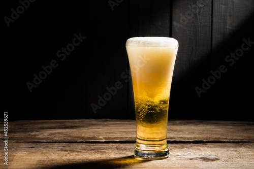 Beer glass with white beer foam on wooden floor dark wood background