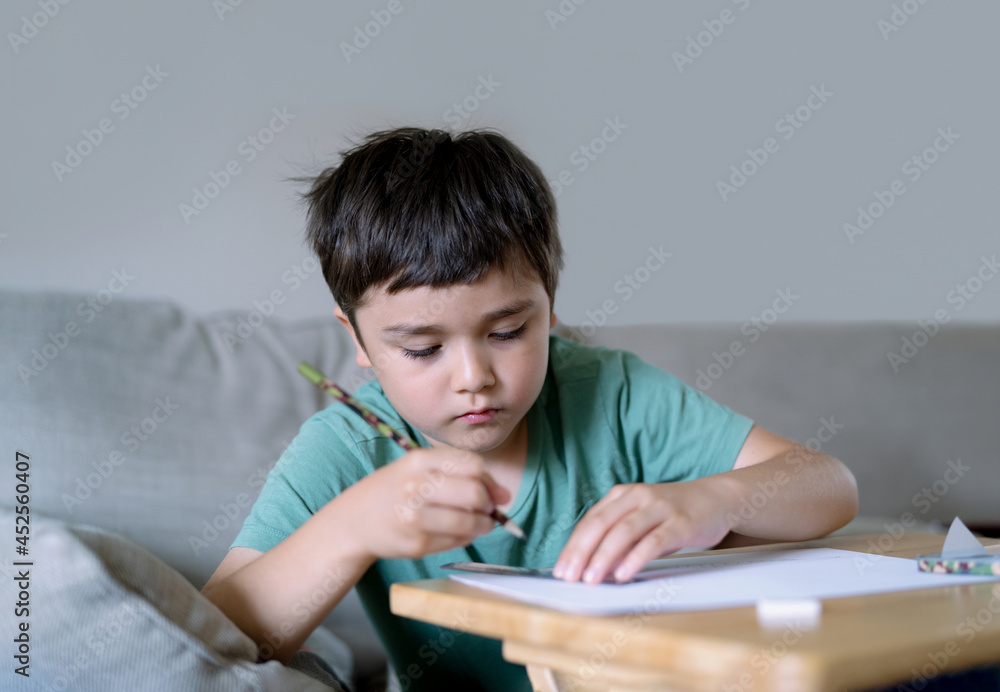 Schoolboy using pencil drawing on white paper sheet, Young kid doing school homework, Happy mixed race child enjoy doing arts and crafts at home on weekend. Home Education Schoolboy using pencil drawing on white paper sheet, Young kid doing school homework, Happy mixed race child enjoy doing arts and crafts at home on weekend. Home Education