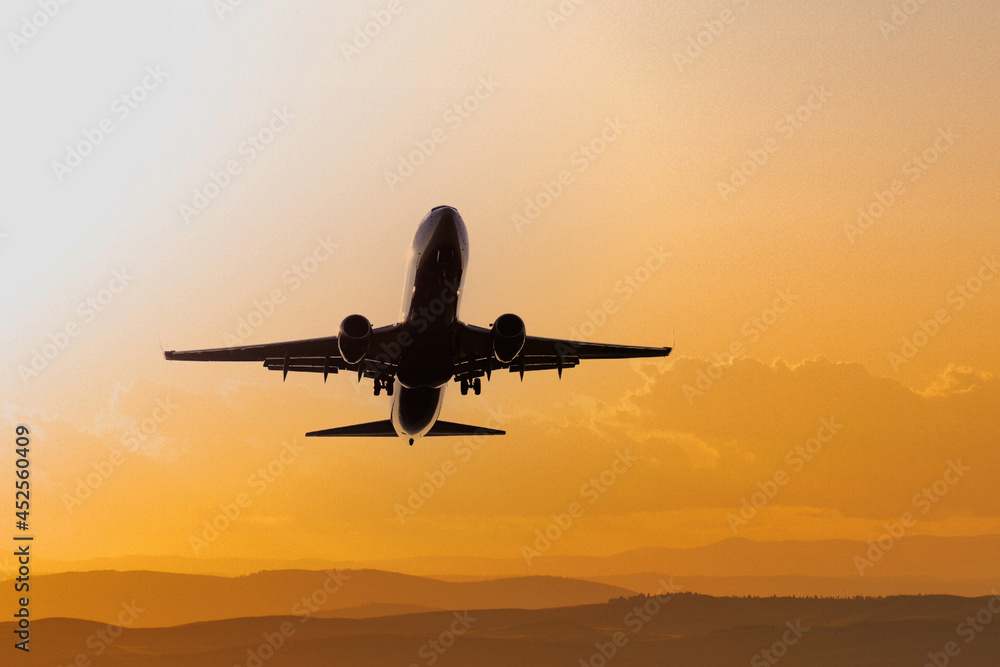 Black silhouette aircraft in the orange sunset sky. Commercial airliner in flight. Travel background with copy space