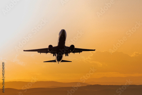 Black silhouette aircraft in the orange sunset sky. Commercial airliner in flight. Travel background with copy space