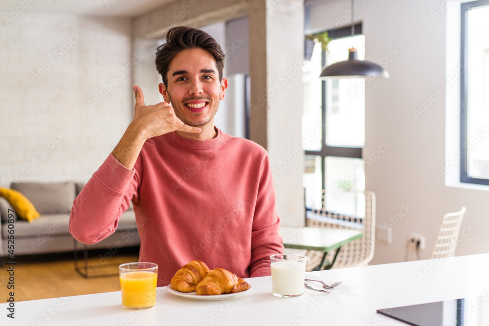 Young mixed race man having breakfast in a kitchen on the morning showing a mobile phone call gesture with fingers. Young mixed race man having breakfast in a kitchen on the morning showing a mobile phone call gesture with fingers.
