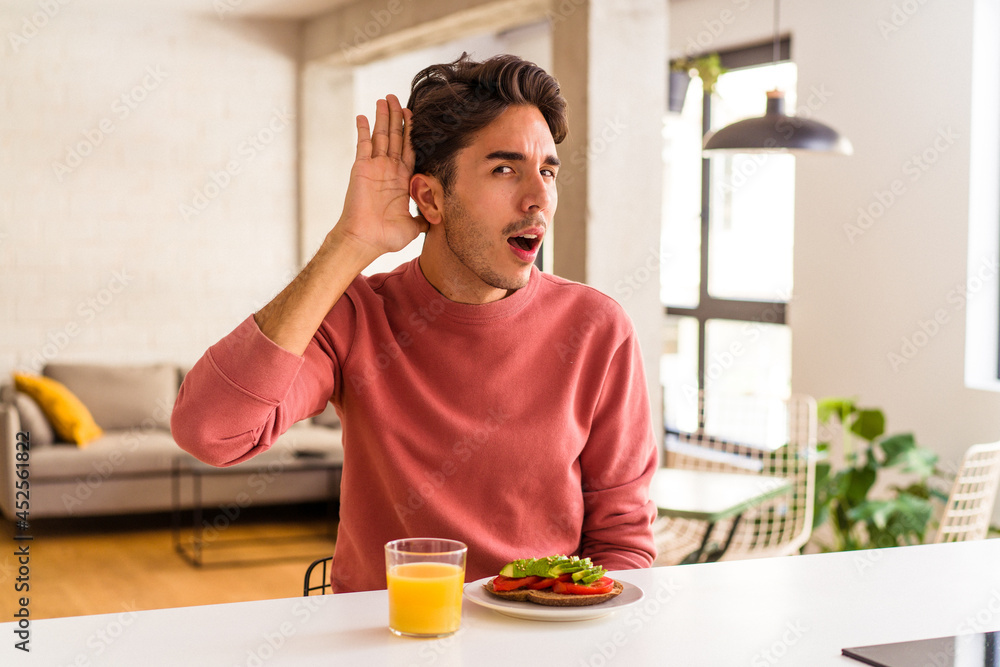 Young mixed race man having breakfast in his kitchen trying to listening a gossip. Young mixed race man having breakfast in his kitchen trying to listening a gossip.