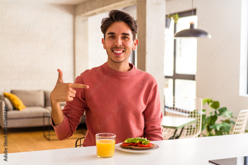 Young mixed race man having breakfast in his kitchen person pointing by hand to a shirt copy space, proud and confident Young mixed race man having breakfast in his kitchen person pointing by hand to a shirt copy space, proud and confident