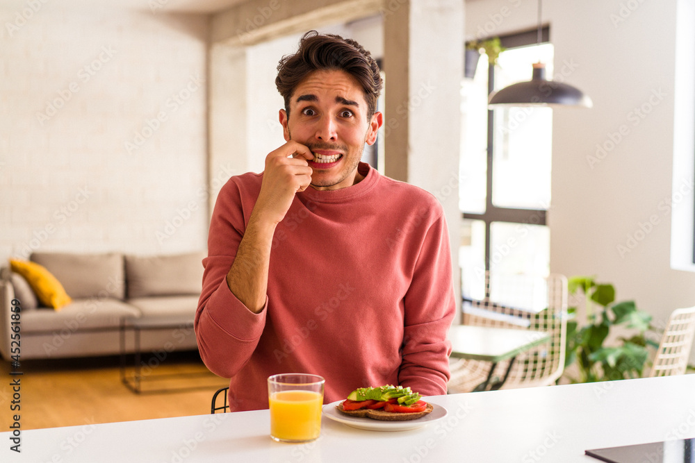 Young mixed race man having breakfast in his kitchen biting fingernails, nervous and very anxious. Young mixed race man having breakfast in his kitchen biting fingernails, nervous and very anxious.