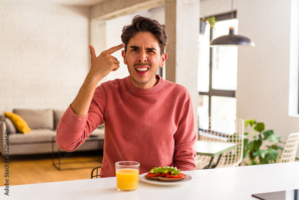 Young mixed race man having breakfast in his kitchen showing a disappointment gesture with forefinger. Young mixed race man having breakfast in his kitchen showing a disappointment gesture with forefinger.