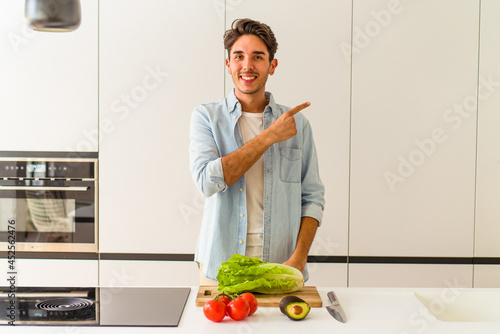 Young mixed race man preparing a salad for lunch smiling and pointing aside, showing something at blank space.