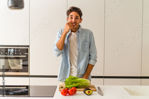 Young mixed race man preparing a salad for lunch biting fingernails, nervous and very anxious.
