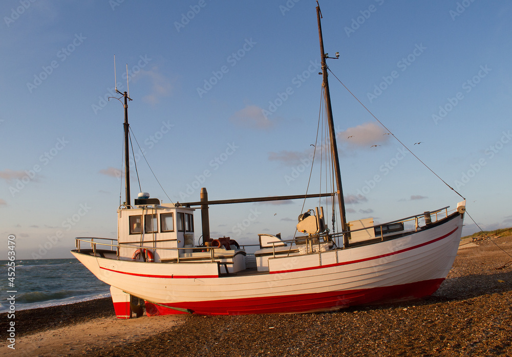 Red and white coastal cutter in the warm light of the sunset, drawn up the beach at Lild Strand in Denmark Red and white coastal cutter in the warm light of the sunset, drawn up the beach at Lild Strand in Denmark
