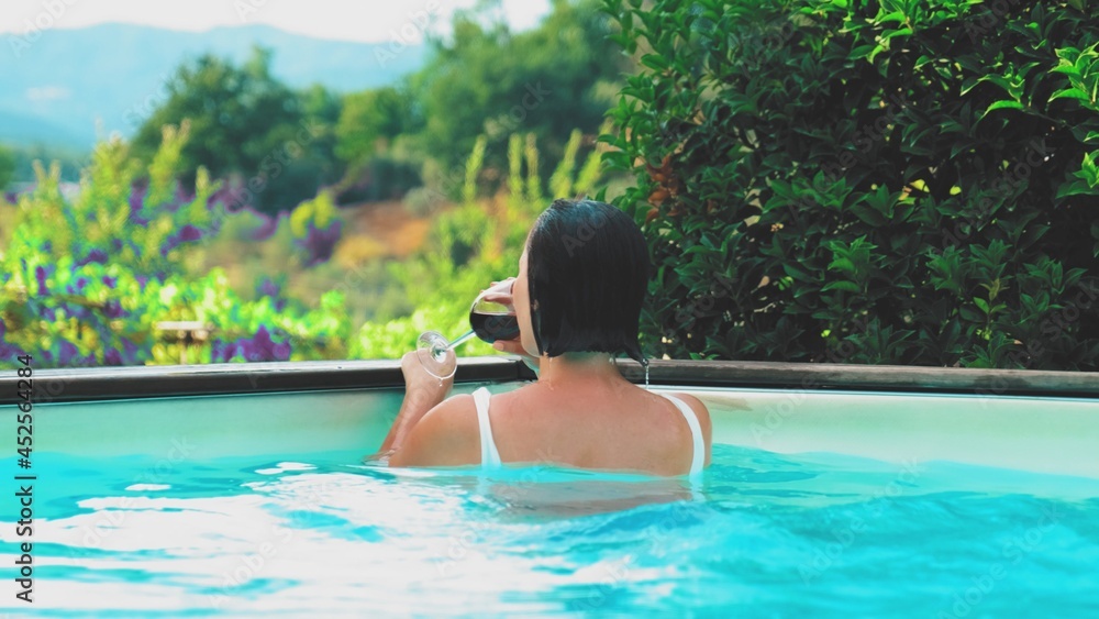 Happy Young Caucasian Woman Enjoying Vacations in Tuscan Resort Swimming in Private Pool and Drinking Red Wine	