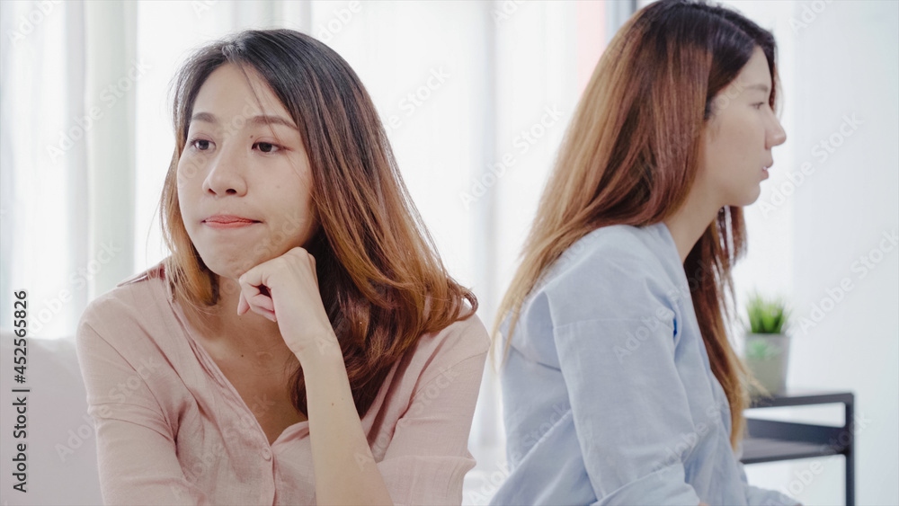 Unhappy Asian lesbian lgbt couple sitting each side of sofa with moody emotion in living room. Women conflict with her girlfriend and have bad relationship at home. Unhappy Asian lesbian lgbt couple sitting each side of sofa with moody emotion in living room. Women conflict with her girlfriend and have bad relationship at home.