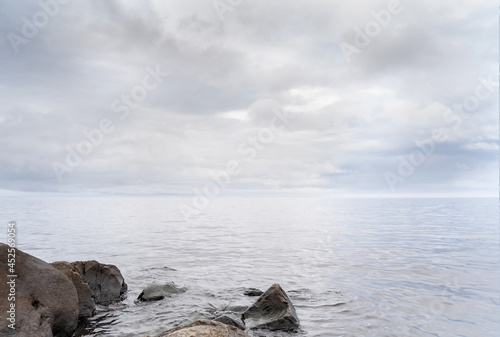 Fotografie Beautiful autumn misty grey lake with rocky shore and cloudy sky at sunset